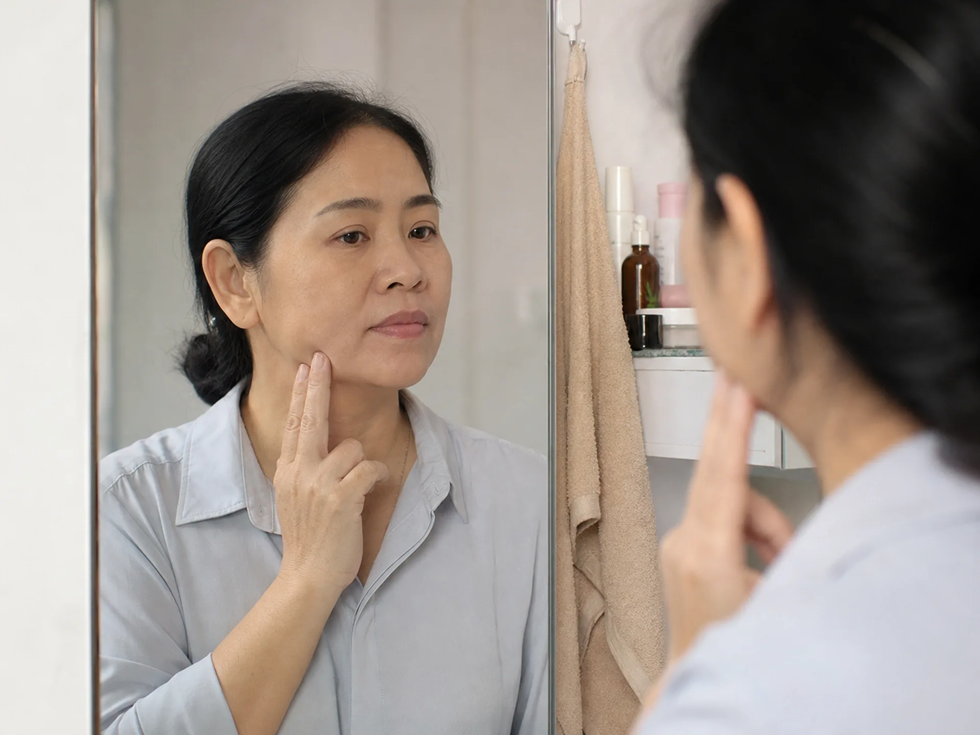 Phụ nữ Việt Nam quan sát đường nét khuôn mặt trước gương, lo lắng da kém săn nhẹ